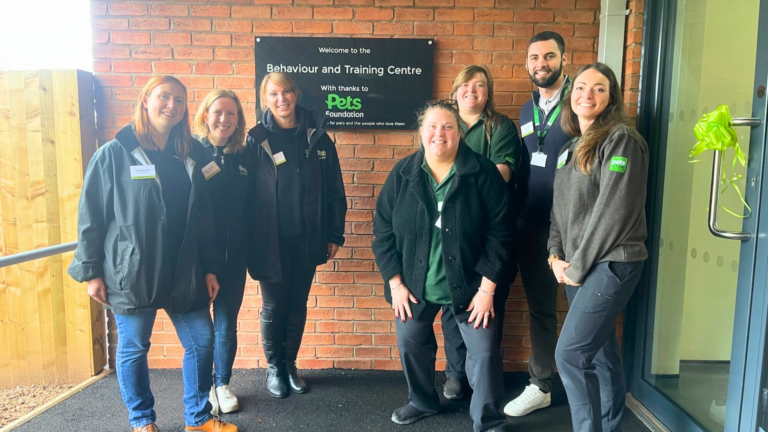 A group of people standing outside a building with a plaque behind them that reads, "Welcome to the Behaviour and Training Centre, With thanks to Pets Foundation, Helping pets and the people who love them.