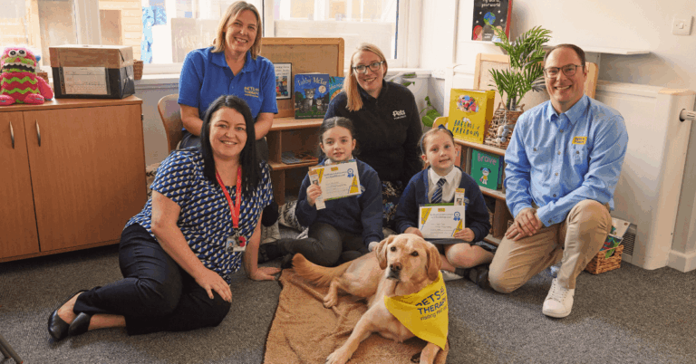 A group of people and a Pets As Therapy dog sitting in a school.