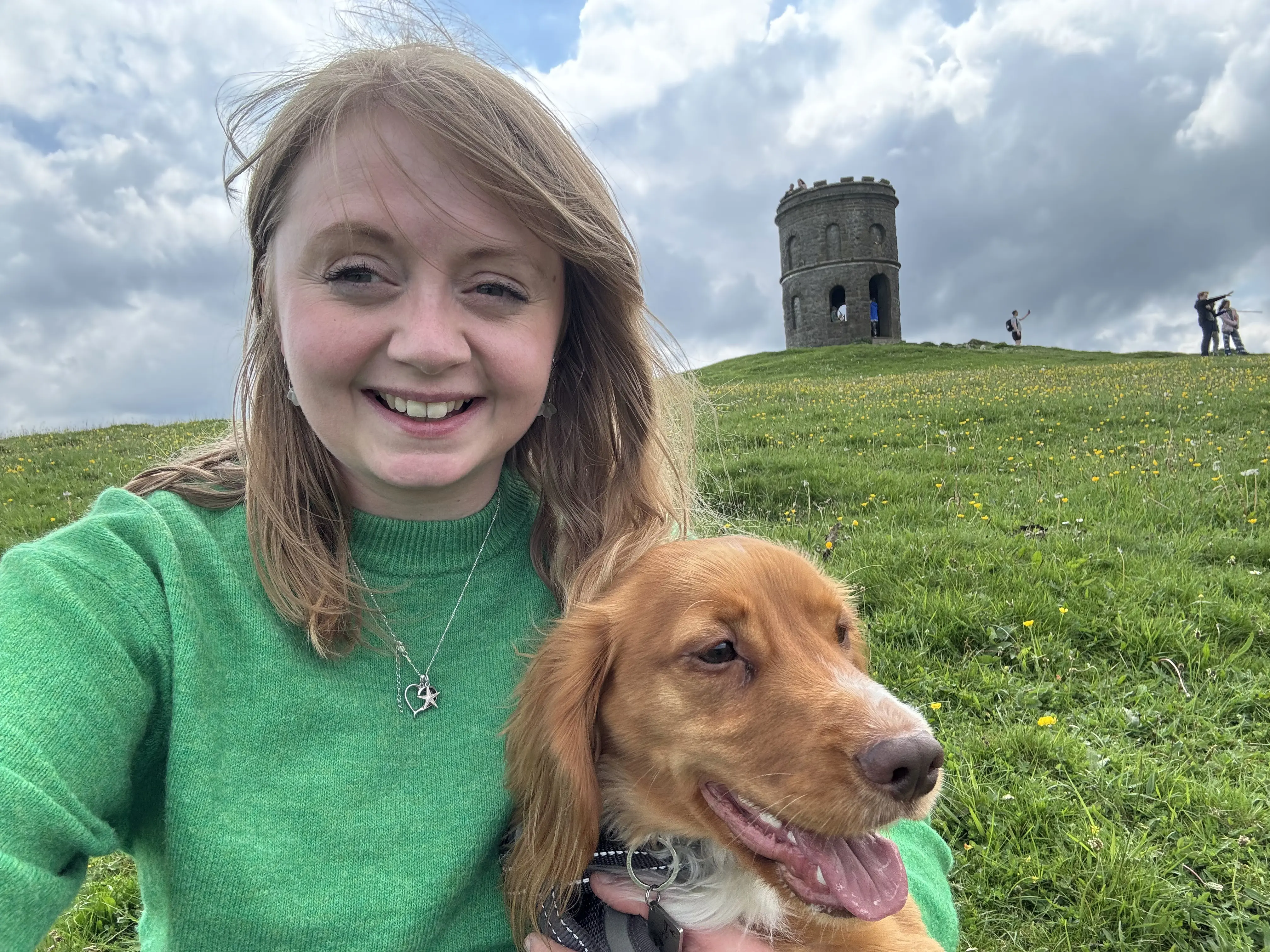 A woman in a green top with an ginger haired dog with a castle in the background.