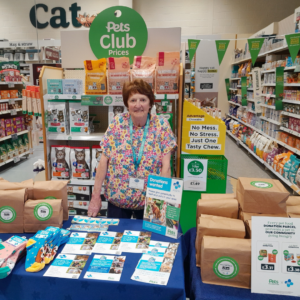 A woman standing behind a display table with pet food parcels in a Pets at home store.