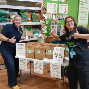 Two women standing next to a display table with pet food parcels in a Pets at Home store.