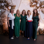 Pets Foundation team standing together at the Foundation Ball indoors in front of large winter-themed Christmas decorations with white, gold and brown garlands, pinecones, ornaments and lights, posing for a group photo.