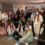Group of people wearing matching black Snore For Paws beanies gathered indoors an animal rescue centre indoors, smiling at the camera for a group photo.