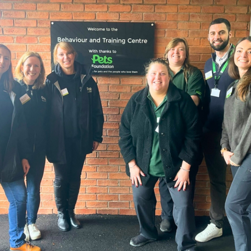 A group of people standing outside a building with a plaque behind them that reads, "Welcome to the Behaviour and Training Centre, With thanks to Pets Foundation, Helping pets and the people who love them.